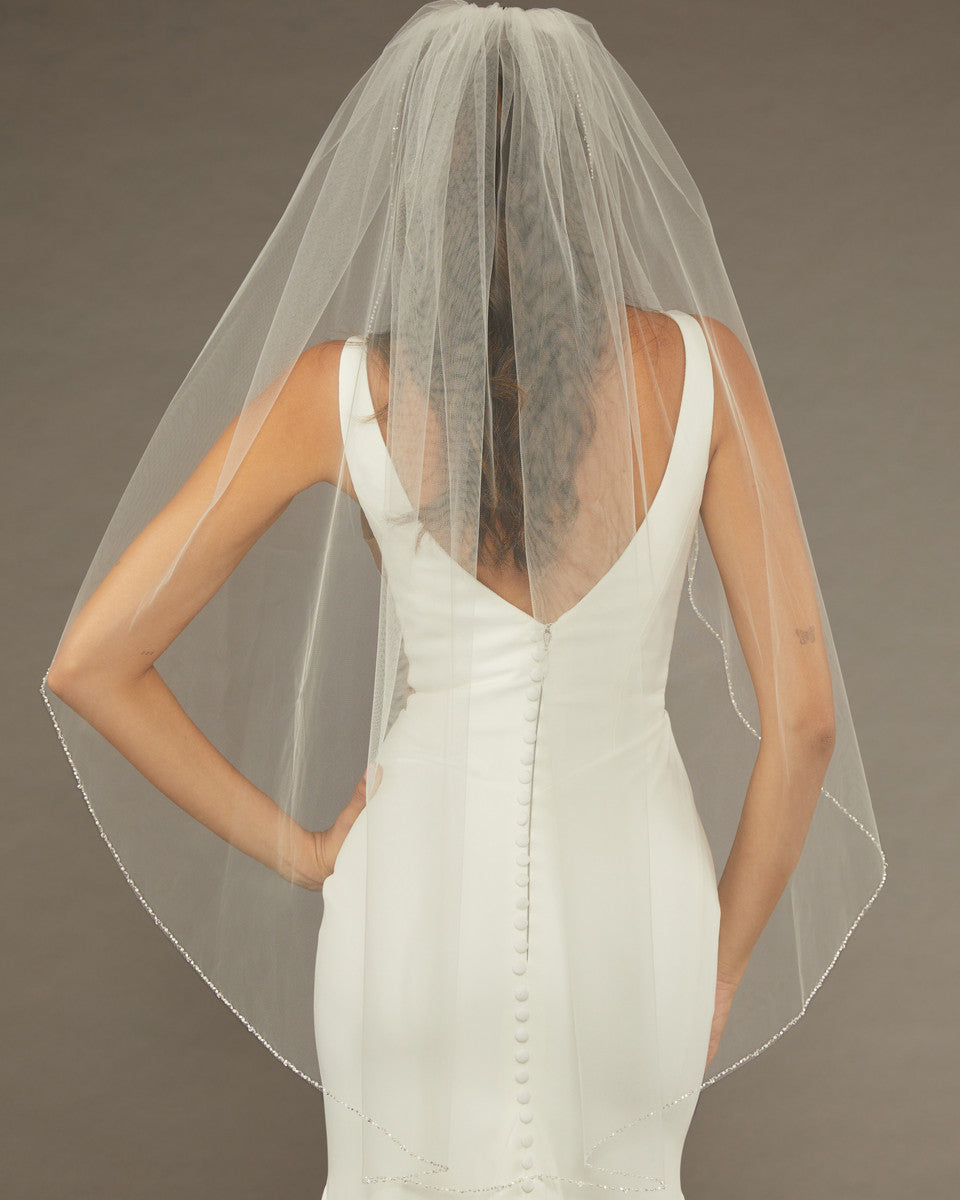 Bridal Veil with Crystal Beads and Pearls Woman wearing a wedding dress with a sheer veil against a brown background