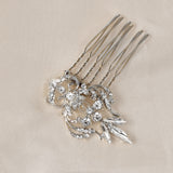 Dainty Regal Wedding Hair Comb A silver-toned hair comb accessory with ornate floral and leaf designs set with clear rhinestones, displayed on a textured beige fabric background.