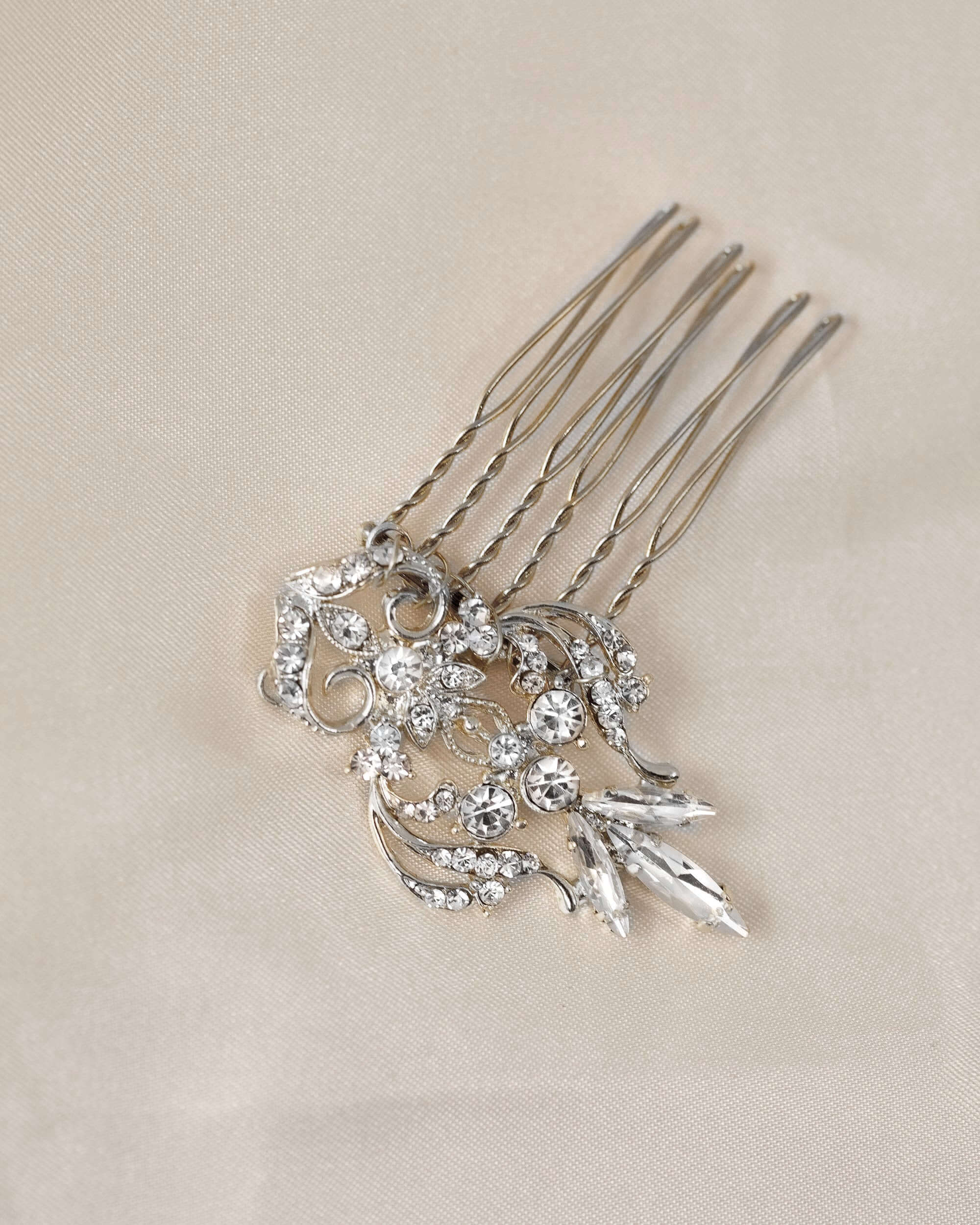 Dainty Regal Wedding Hair Comb A silver-toned hair comb accessory with ornate floral and leaf designs set with clear rhinestones, displayed on a textured beige fabric background.