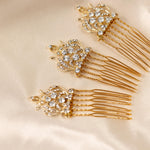 Regal Styled Small Wedding Hair Comb Three gold bridal hair combs embellished with clear rhinestones, arranged diagonally on a cream satin fabric background.