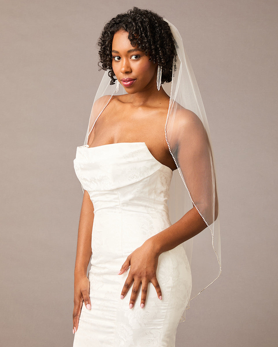 Fingertip Bridal Veil with Rhinestone Chain Trim Woman wearing a  strapless dress with a sheer veil against a plain background