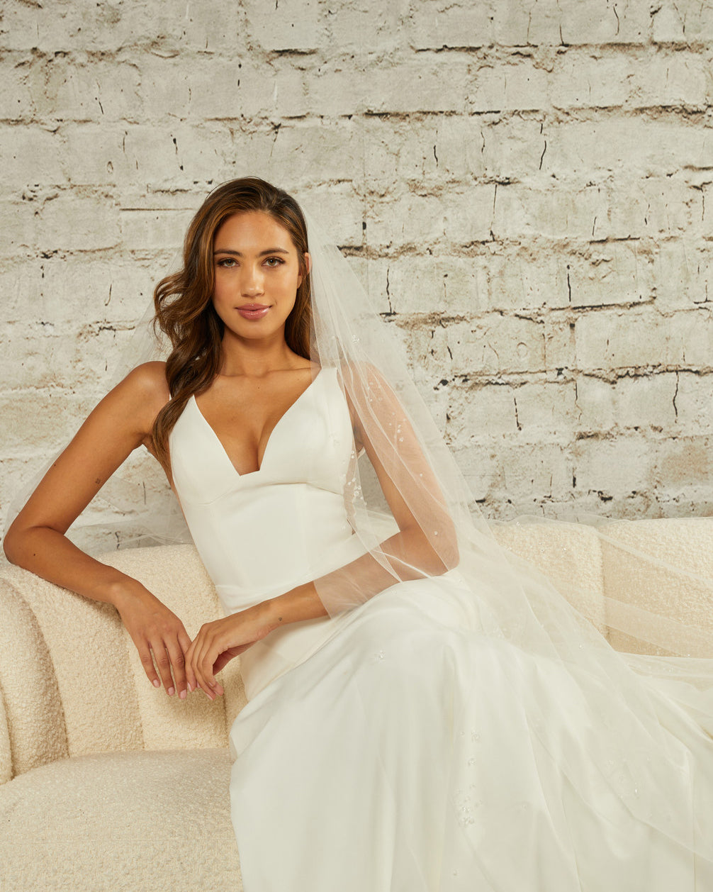 Cathedral Veil with Scattered Clusters of Crystal Beads Woman in a  wedding dress sitting on a couch against a brick wall.