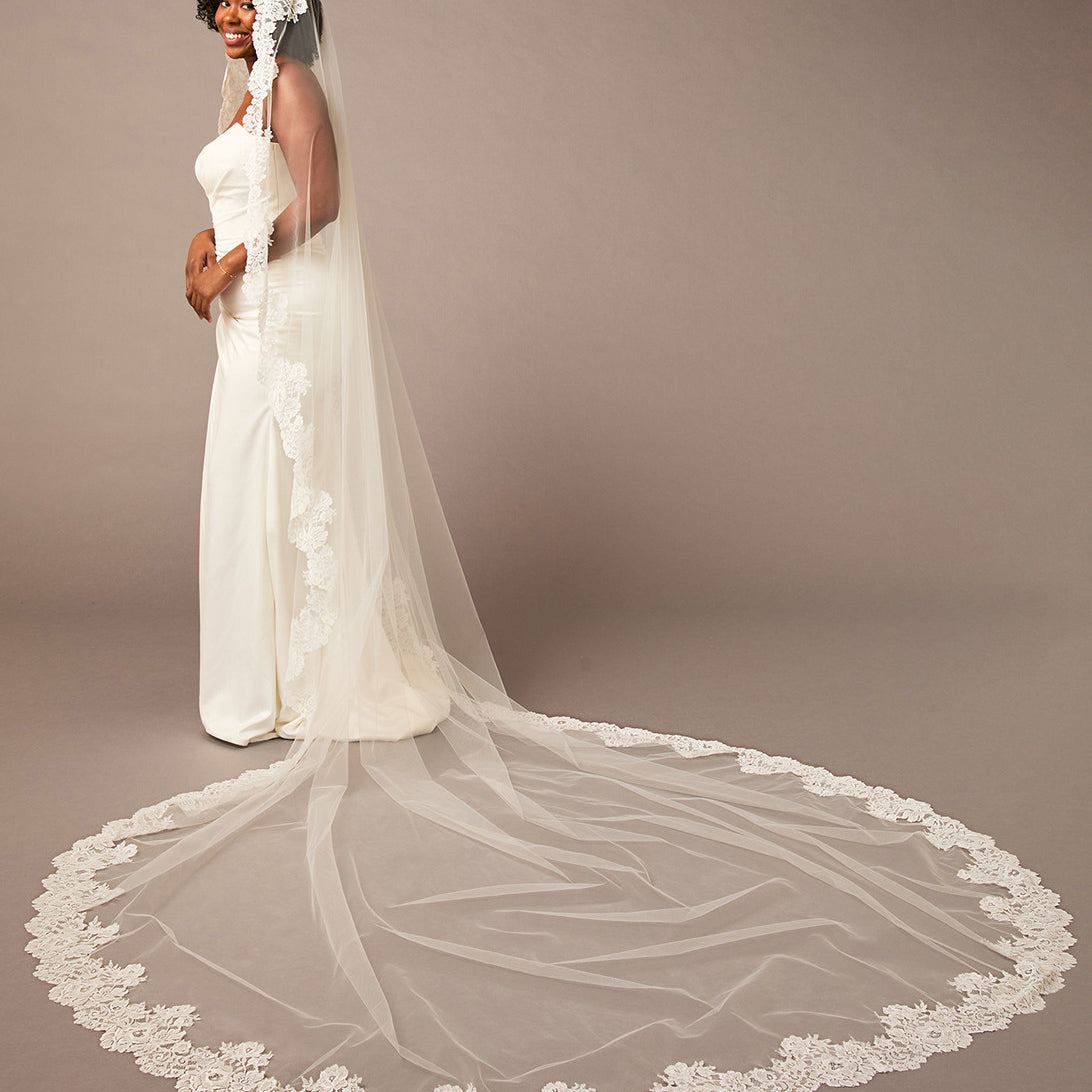 Woman wearing a long white wedding veil with lace details on a brown  Mantilla Cathedral Veil with Wide Flower Chantilly Lacebackground
