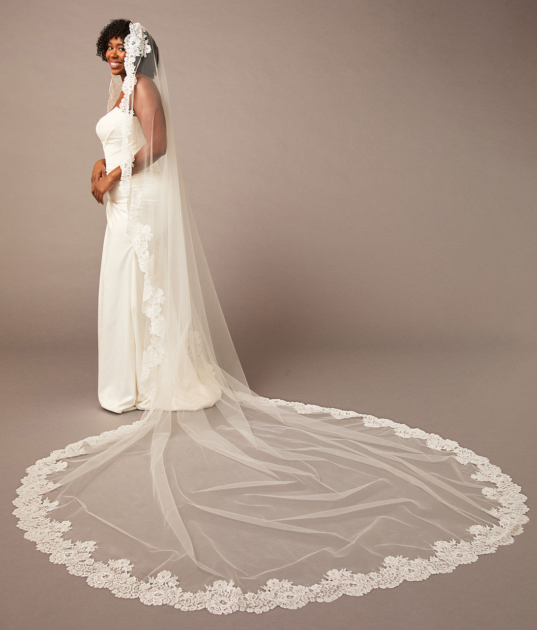 Woman wearing a long white wedding veil with lace details on a brown  Mantilla Cathedral Veil with Wide Flower Chantilly Lacebackground
