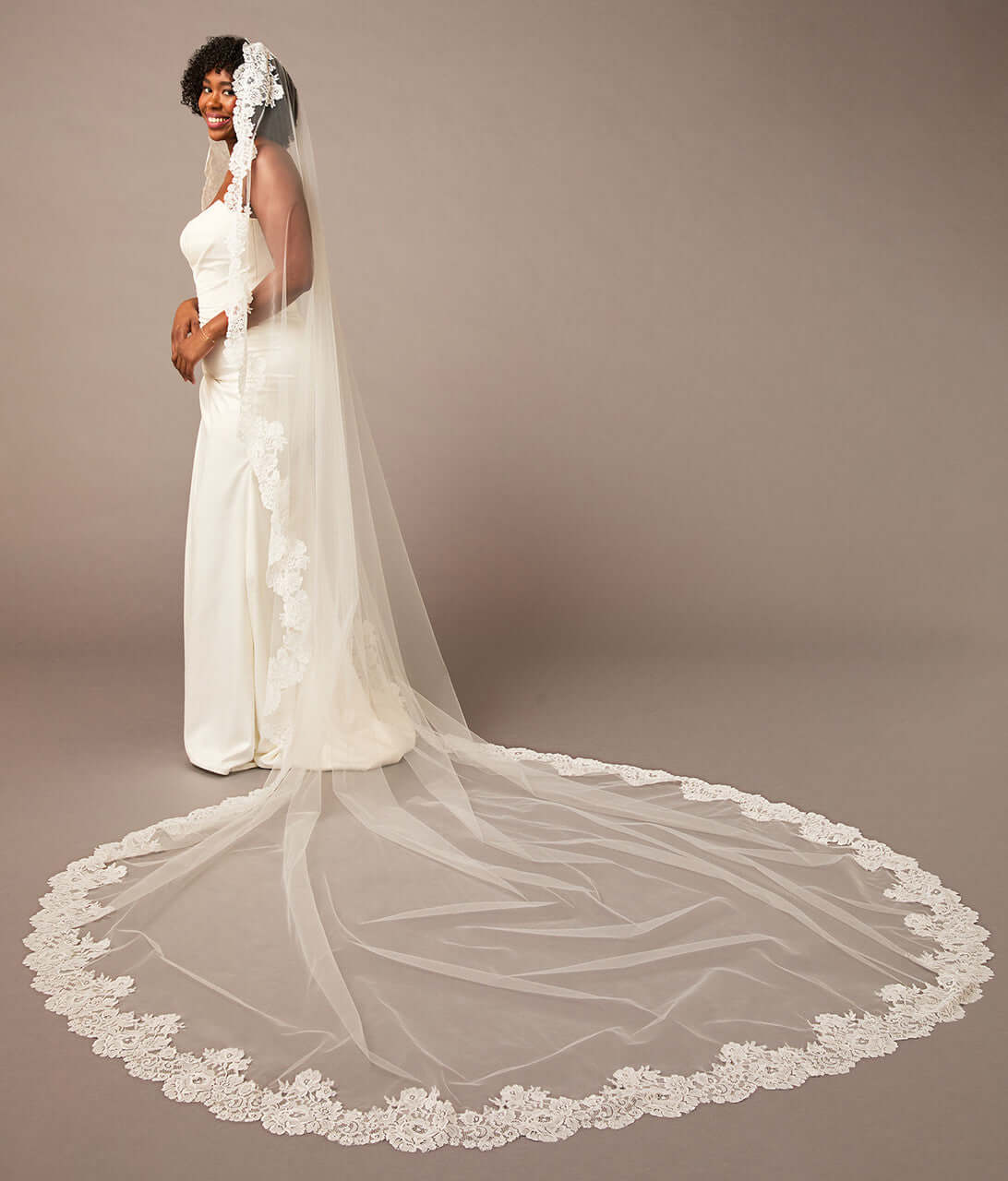Woman wearing a long white wedding veil with lace details on a brown  Mantilla Cathedral Veil with Wide Flower Chantilly Lacebackground