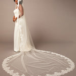 Woman wearing a long white wedding veil with lace details on a brown  Mantilla Cathedral Veil with Wide Flower Chantilly Lacebackground