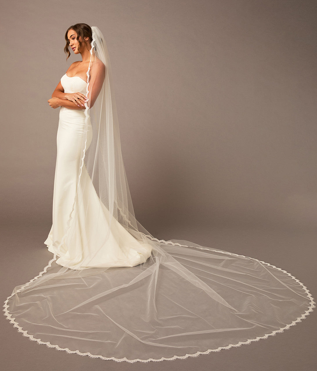  Bridal Veil with Scalloped Small Eyelash Lace Woman wearing a white wedding dress with a long veil against a plain background