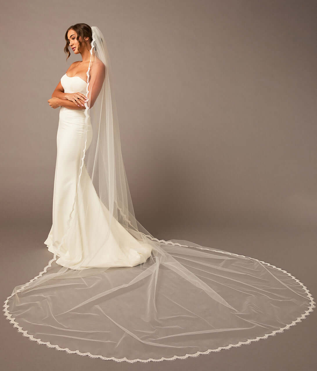  Bridal Veil with Scalloped Small Eyelash Lace Woman wearing a white wedding dress with a long veil against a plain background