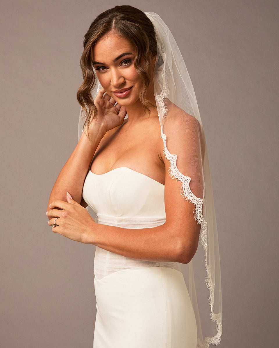 Bridal Veil with Scalloped Small Eyelash Lace Woman wearing a white wedding dress with a lace veil against a brown background