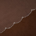 Cathedral Veil with Oat Pearl Scallop Edge A close-up of a brown textured fabric with a decorative wavy border featuring small white floral motifs and clear rhinestone accents.