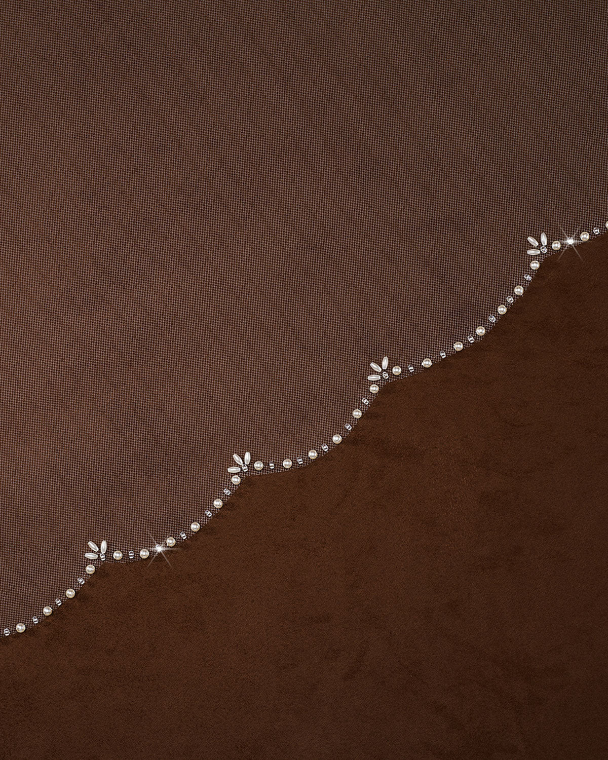 Cathedral Veil with Oat Pearl Scallop Edge A close-up of a brown textured fabric with a decorative wavy border featuring small white floral motifs and clear rhinestone accents.