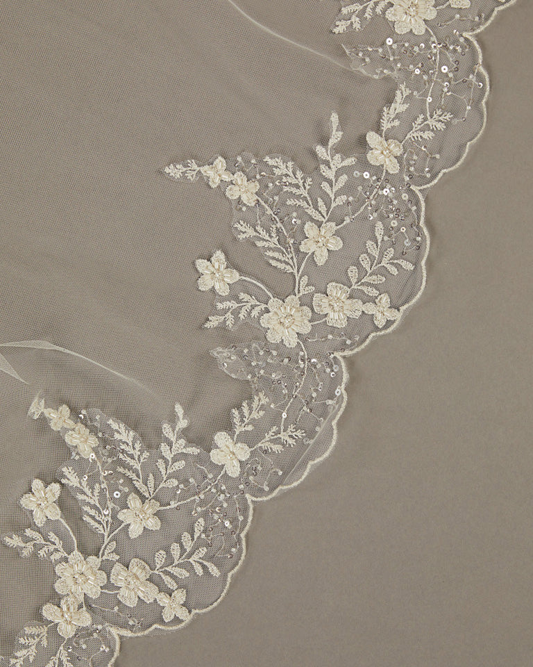 Cathedral Wedding Veil Finished Scallop Edge and Beads Close-up of lace fabric with floral patterns on a beige background