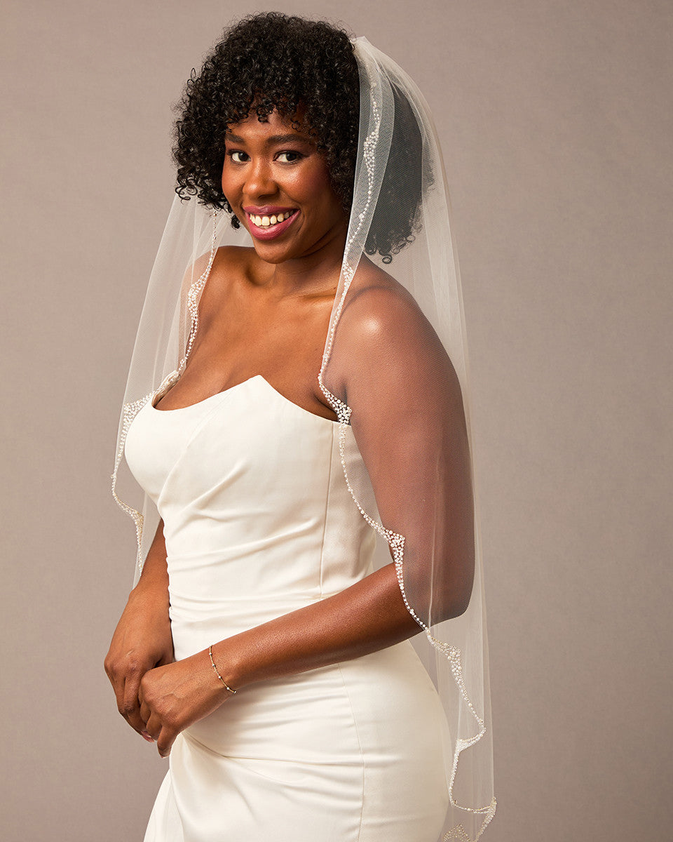 Scalloped Bridal Veil Covered in Pearls and Beads Woman wearing a wedding dress with a veil against a plain background