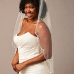 Scalloped Bridal Veil Covered in Pearls and Beads Woman wearing a wedding dress with a veil against a plain background