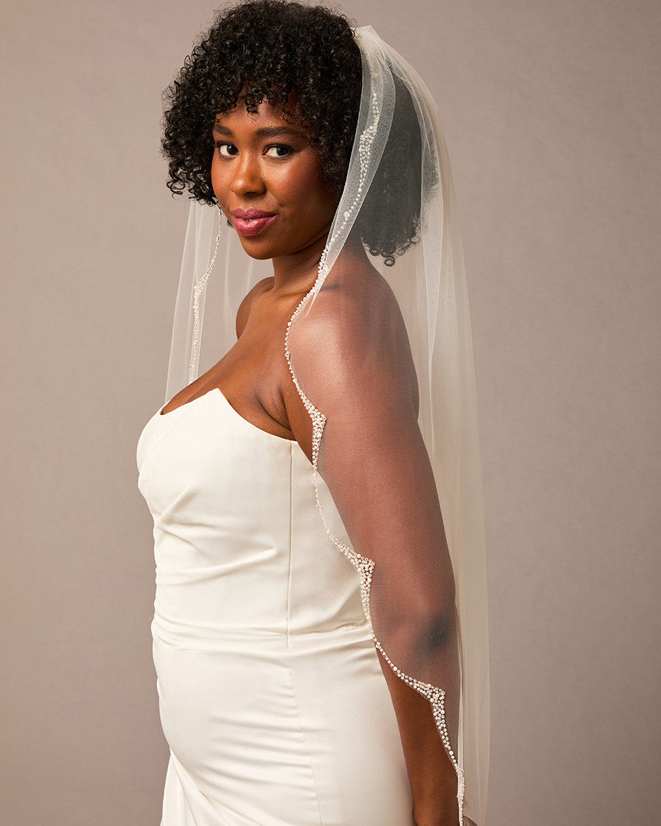 Scalloped Bridal Veil Covered in Pearls and Beads Woman wearing a wedding dress with a veil against a plain background