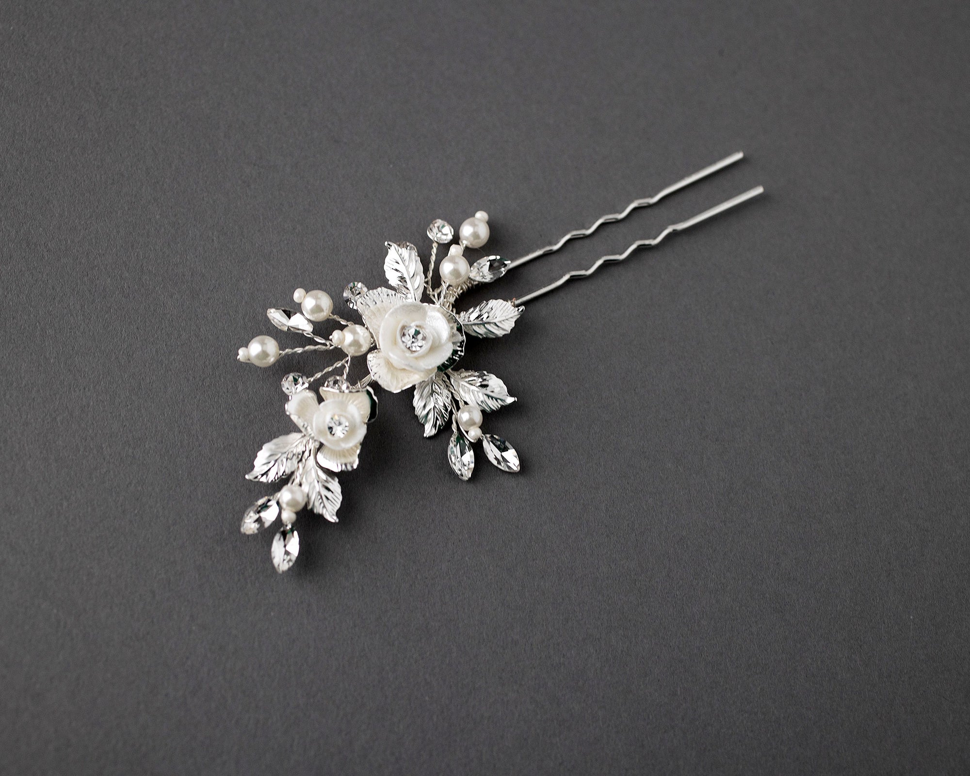 This stunning hair pin features bright porcelain flowers in ivory, adorned with marquise crystal stones for a sophisticated look that adds a subtle sparkle to your bridal hairstyle. Crafted from silver or light gold leaves and petals, this decorative piece measures 2.75 by 1.75 inches, making it the perfect choice for any blushing bride.
