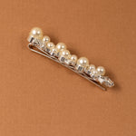 Bridal Bobby Pin with Ivory Pearls A silver hair claw clip embellished with a row of cream-colored faux pearls and clear rhinestones, displayed diagonally on a textured brown background.