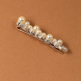 Bridal Bobby Pin with Ivory Pearls A silver hair claw clip embellished with a row of cream-colored faux pearls and clear rhinestones, displayed diagonally on a textured brown background.