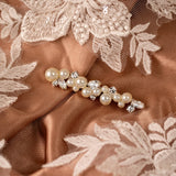 Bridal Bobby Pin with Ivory Pearls A close-up of a pearl and crystal hair accessory laid on warm taupe satin fabric with white floral lace embroidery.