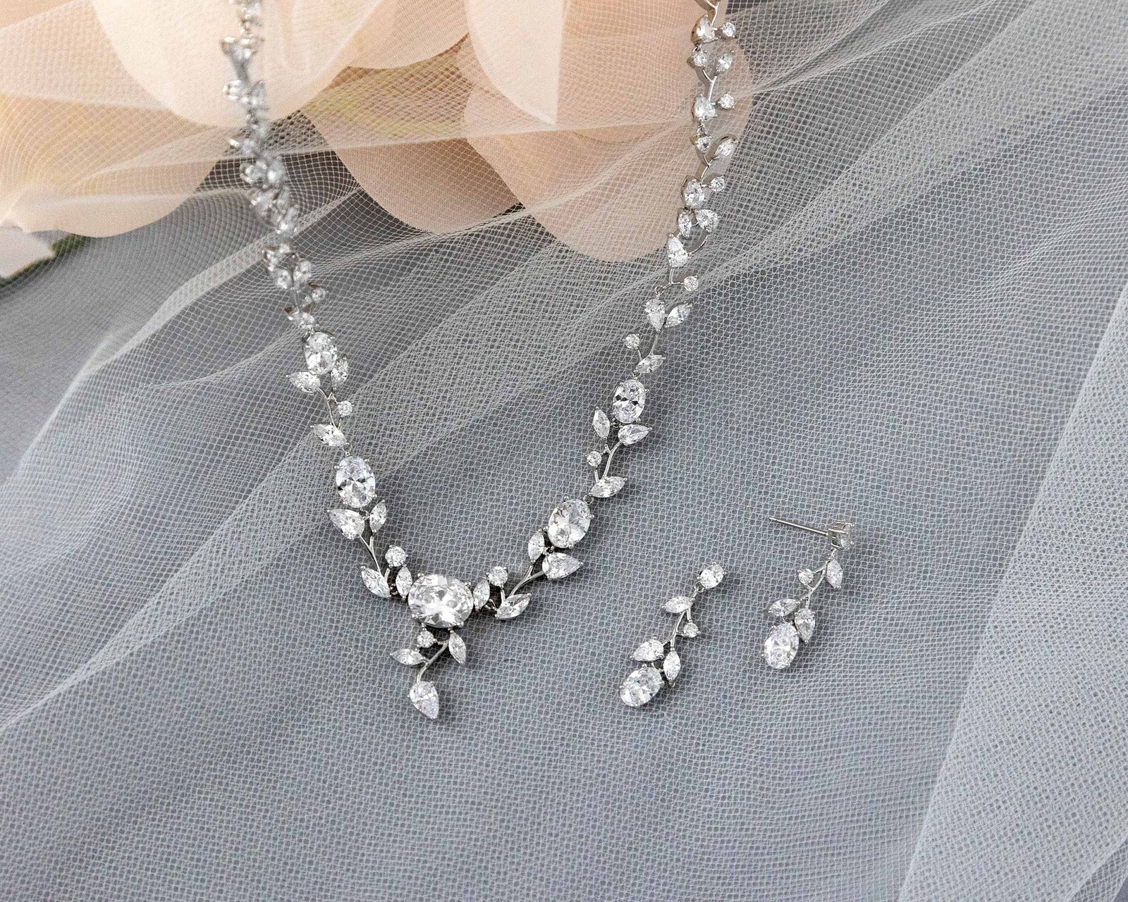A bridal necklace set with dainty oval vines and sparkling oval CZ gems, displayed on a translucent fabric surface.