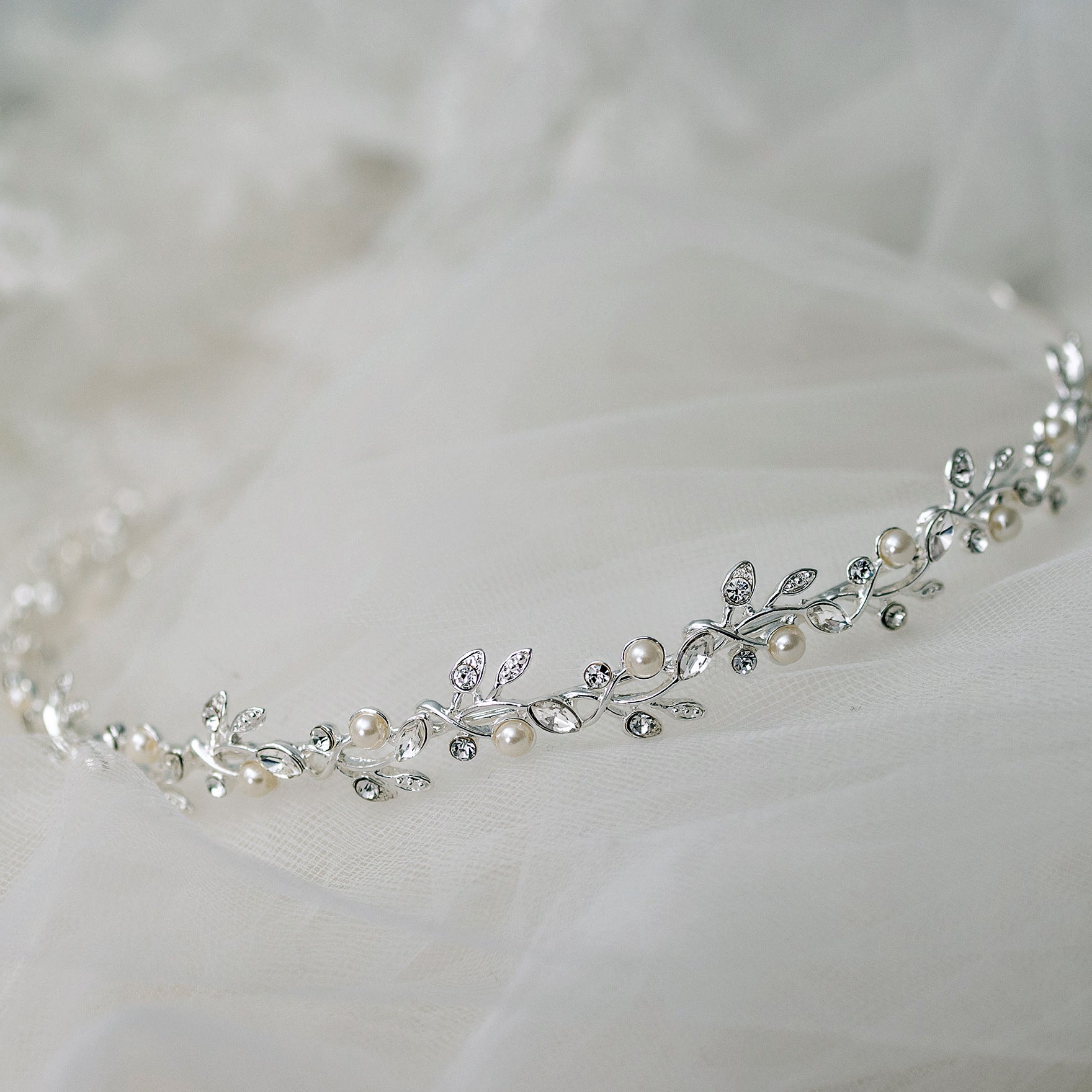 Silver tiara with pearls and crystals on a white fabric background