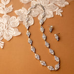 Pearl and crystal necklace with matching earrings on a brown background with lace fabric.