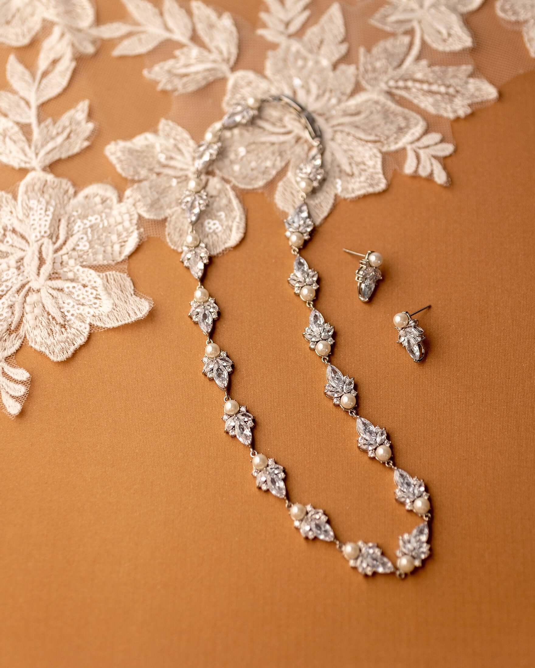Pearl and crystal necklace with matching earrings on a brown background with lace fabric.