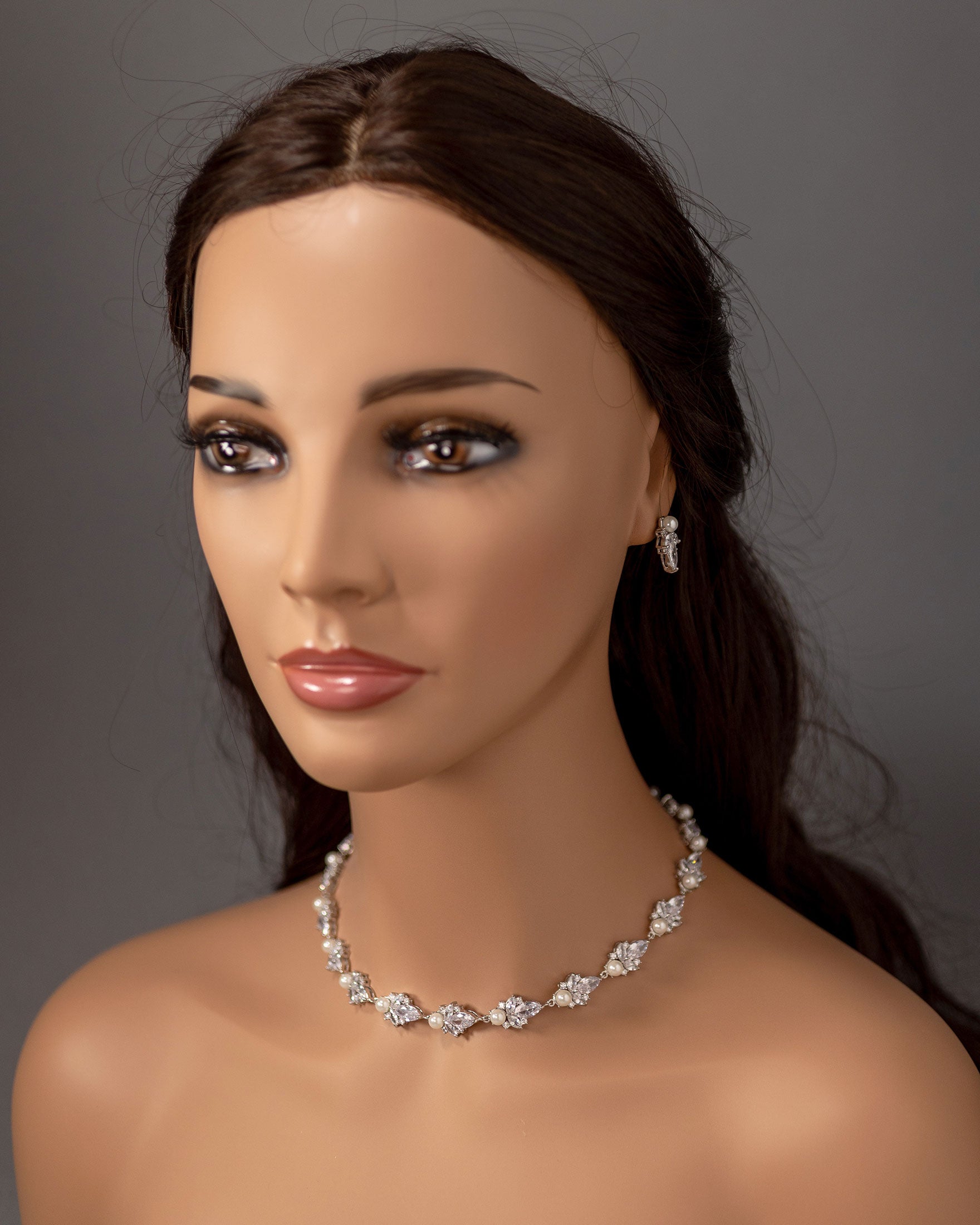 Mannequin head with a cz necklace and earrings on a gray background