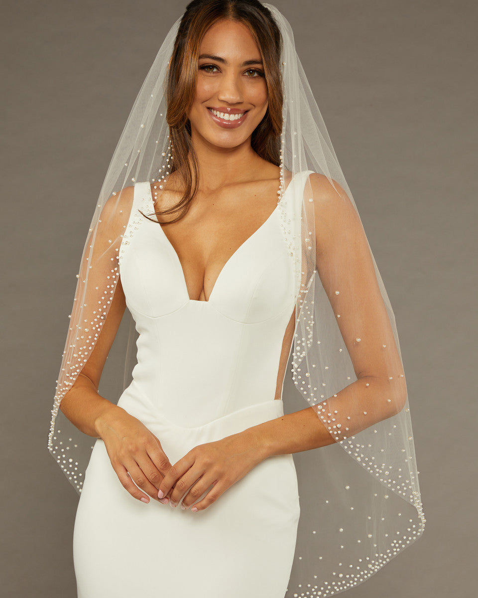 Fingertip Veil with Dense Scatter of Pearls Woman wearing a wedding dress with a veil against a brown background