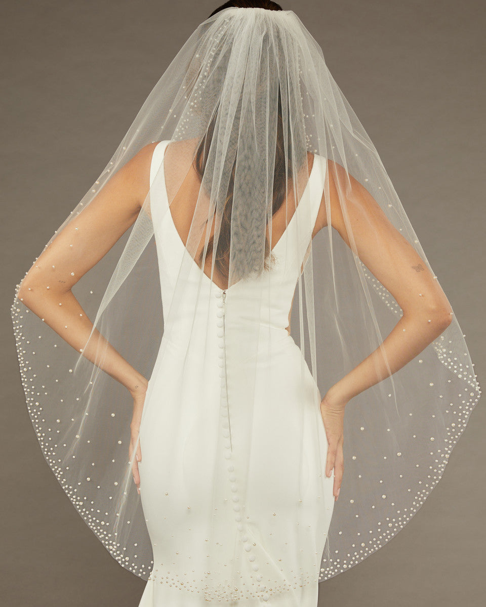Fingertip Veil with Dense Scatter of Pearls Bride wearing a wedding dress with a sheer veil against a neutral background