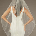 Fingertip Veil with Dense Scatter of Pearls Bride wearing a wedding dress with a sheer veil against a neutral background