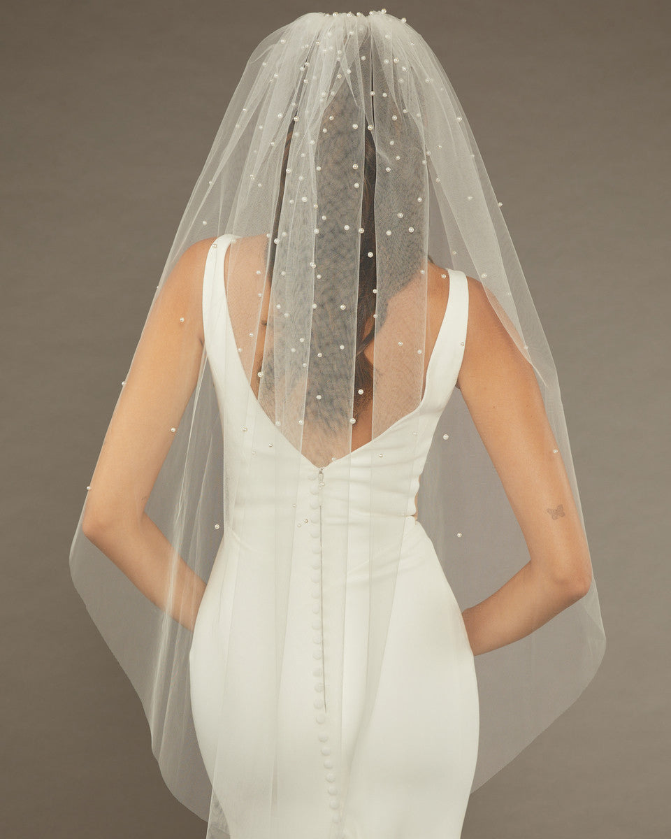 Reverse Pearl Scatter Bridal Veil Bride wearing a wedding dress with a sheer veil against a brown background