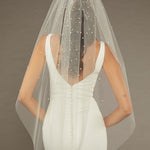 Reverse Pearl Scatter Bridal Veil Bride wearing a wedding dress with a sheer veil against a brown background