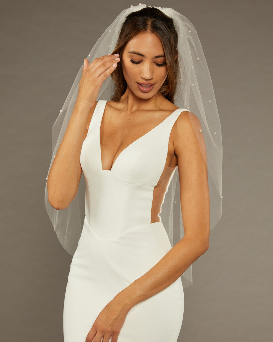 Reverse Pearl Scatter Bridal Veil Woman wearing a wedding dress with a sheer veil against a brown background