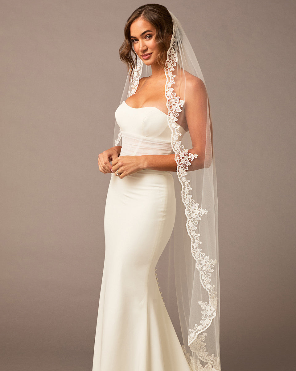 Waltz Wedding Veil with Alencon Lace Woman wearing a white wedding dress with a lace veil against a brown background