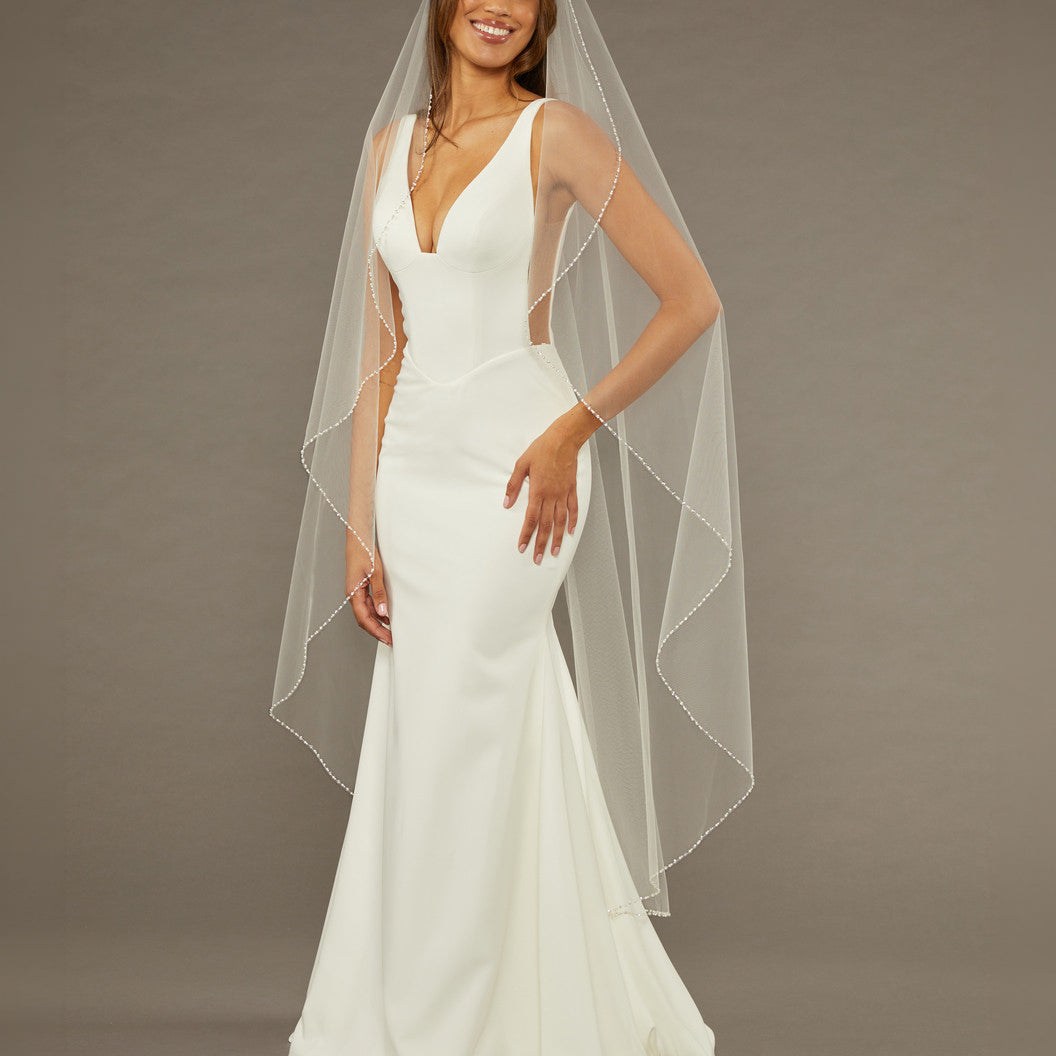 Waltz Waterfall Veil with Pearls and Sequins Woman wearing a wedding dress with a long veil against a brown background