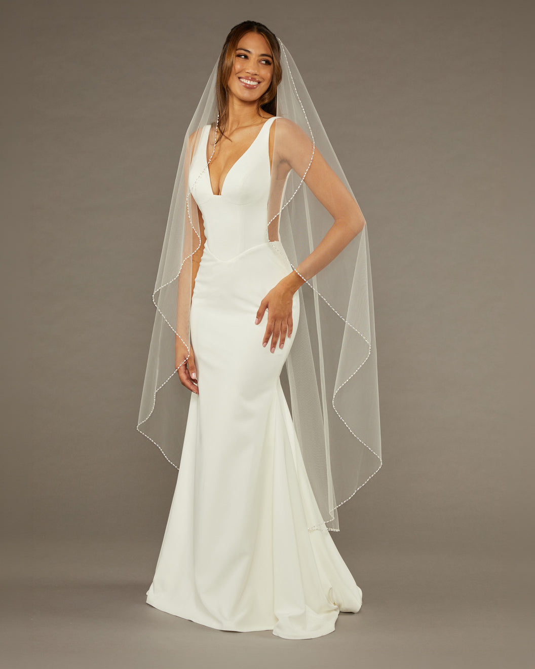 Waltz Waterfall Veil with Pearls and Sequins Woman wearing a wedding dress with a long veil against a brown background