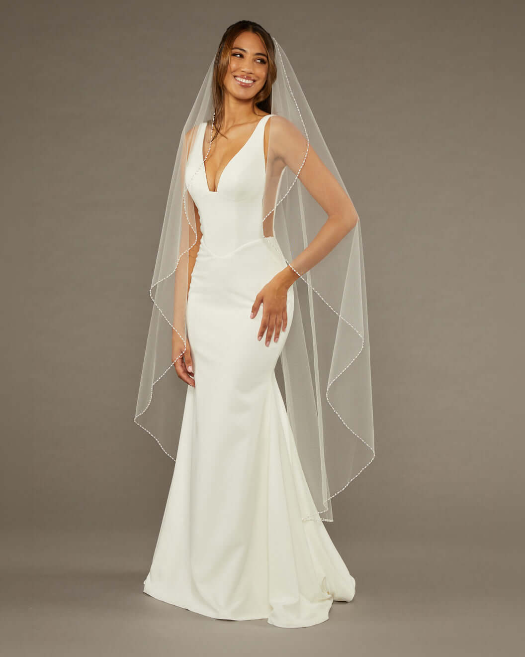 Waltz Waterfall Veil with Pearls and Sequins Woman wearing a wedding dress with a long veil against a brown background