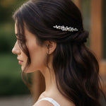 Bridal Bobby Pin with Marquise Jewels & Pearls A woman in profile with long dark brown hair wearing a delicate silver bridal hair accessory with clear stones, set against a softly blurred warm-toned background.