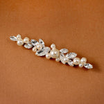 Bridal Bobby Pin with Marquise Jewels & Pearls A floral bridal hair clip featuring faux pearls and clear rhinestones, displayed diagonally on a warm brown textured background.