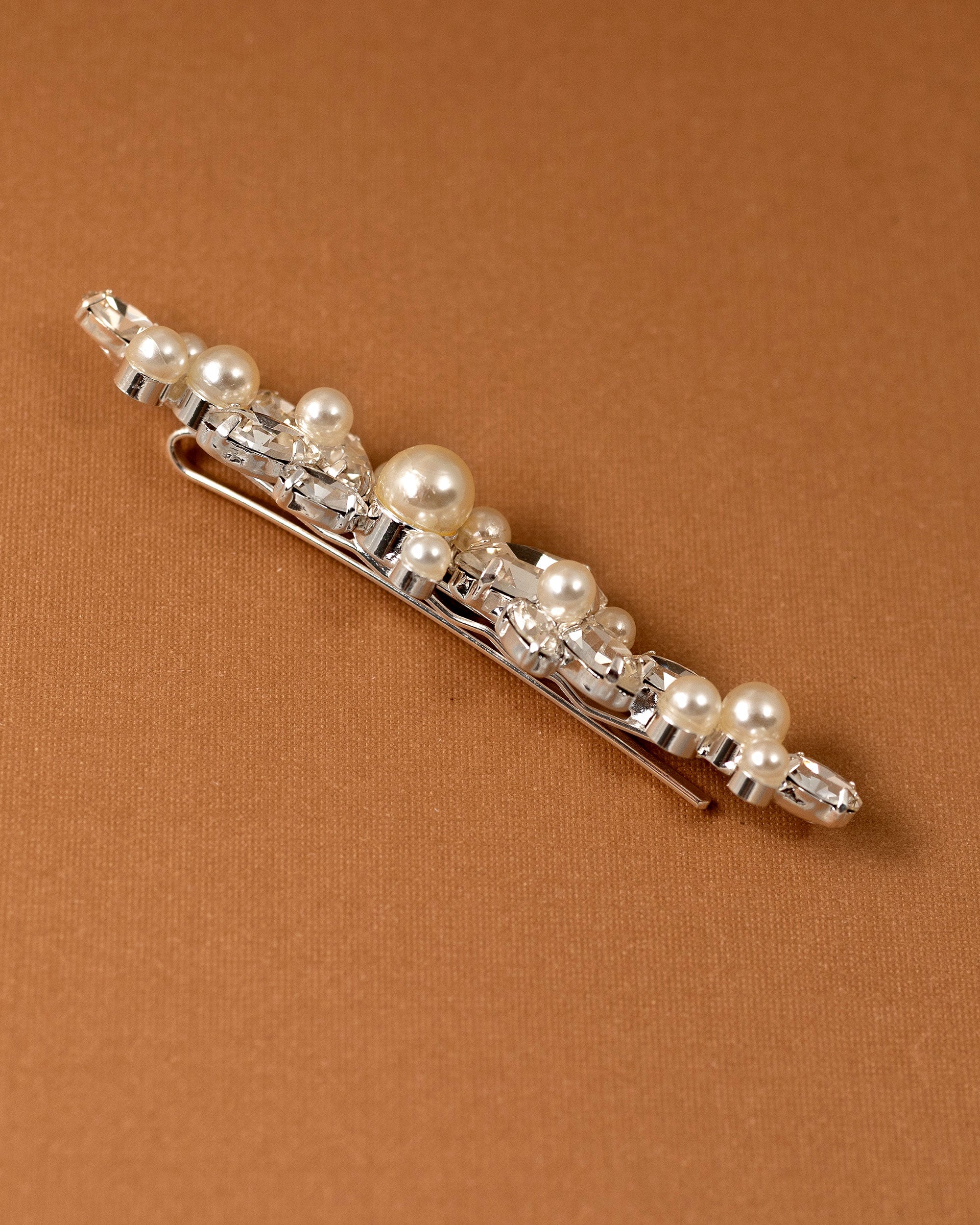 Bridal Bobby Pin with Marquise Jewels & Pearls A silver hair claw clip embellished with faux pearls and clear rhinestones, displayed diagonally on a textured brown background.