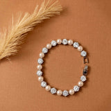 Pearl Bracelet Alternating CZ Stones A pearl and crystal beaded bracelet arranged in a circle on a warm brown textured background, with a dried grass stem in the upper left corner.