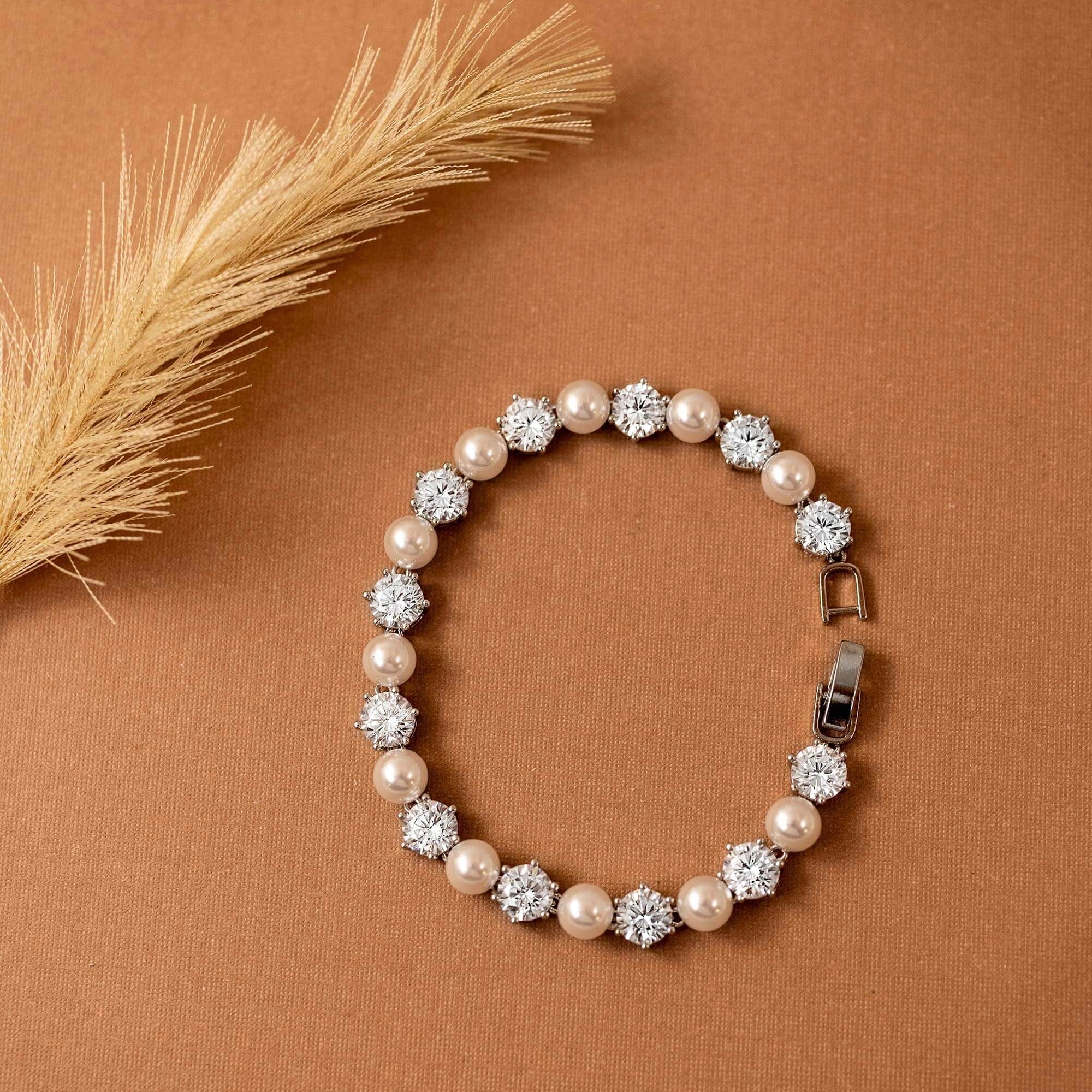 Pearl Bracelet Alternating CZ Stones A pearl and crystal beaded bracelet arranged in a circle on a warm brown textured background, with a dried grass stem in the upper left corner.