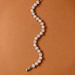 Pearl Bracelet Alternating CZ Stones A curved tennis bracelet featuring cream-colored pearls and clear round-cut gemstones in silver-toned settings, displayed on a textured brown background.