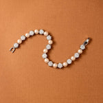 Pearl Bracelet Alternating CZ Stones A pearl and crystal tennis bracelet arranged in a curved S-shape on a textured brown background.