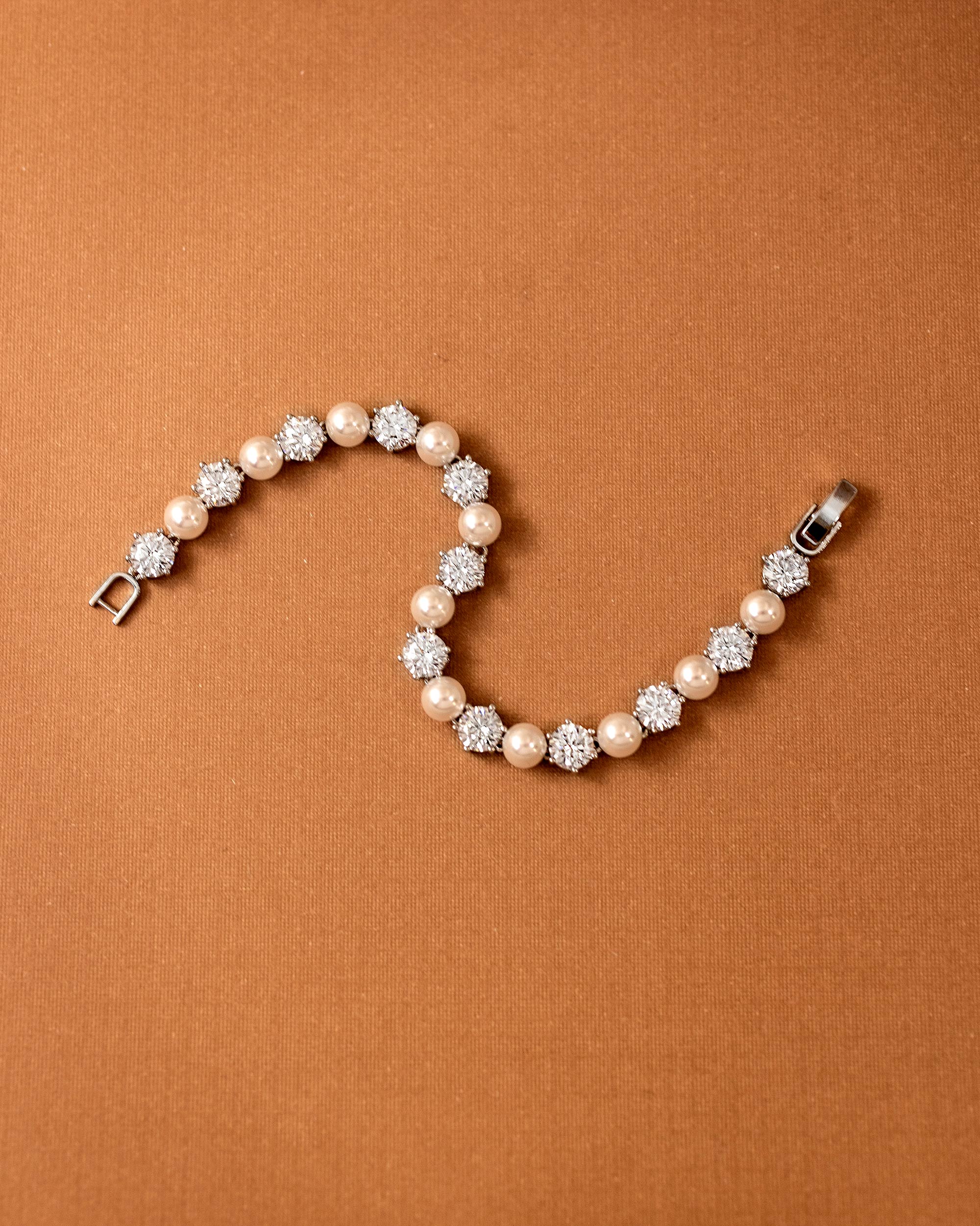 Pearl Bracelet Alternating CZ Stones A pearl and crystal tennis bracelet arranged in a curved S-shape on a textured brown background.