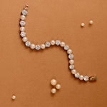 Pearl Bracelet Alternating CZ Stones A pearl and crystal bracelet arranged in a curved S-shape on a textured orange-brown background, with a few loose pearl-like beads scattered nearby.