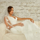 Regal Length Wedding Veil with 3D Organza Flowers Woman in a wedding dress sitting on a couch with a white brick wall background