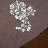 Bridal Luxe Veil with Painted Flowers Cassandra Lynne  A close-up of a sheer taupe mesh fabric with a white floral print, layered over a darker brown textured surface.