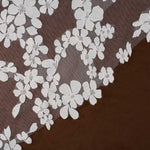 Light ivory floral lace trim with embroidered cherry blossom motifs over a sheer brown mesh, shown laid diagonally on a dark brown surface.